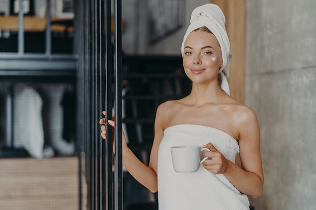 Mooie ontspannen vrouw gewikkeld in handdoek thee drinken