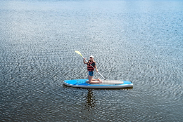 Mooie opgepompte atleet poseert op het water op een bord en vangt de zonnestralen op haar lichaam Het concept van extreme sporten