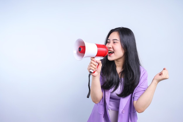Mooie opgewonden Aziatische vrouw schreeuwt en houdt een megafoon vast terwijl ze de hand knijpt