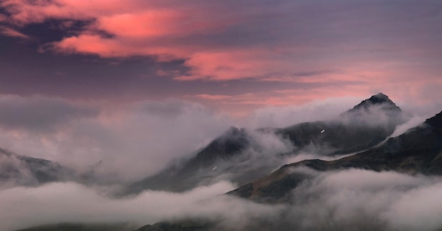 Mooie opname van bergtoppen bedekt met wolken met de avondroze zonsondergang die de hemel verlicht