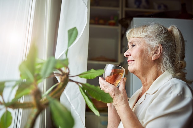 Mooie oude vrouw die thuis kruidenthee drinkt