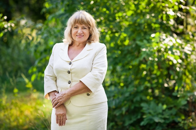 Mooie oude vrouw in een wit pak glimlacht in het park