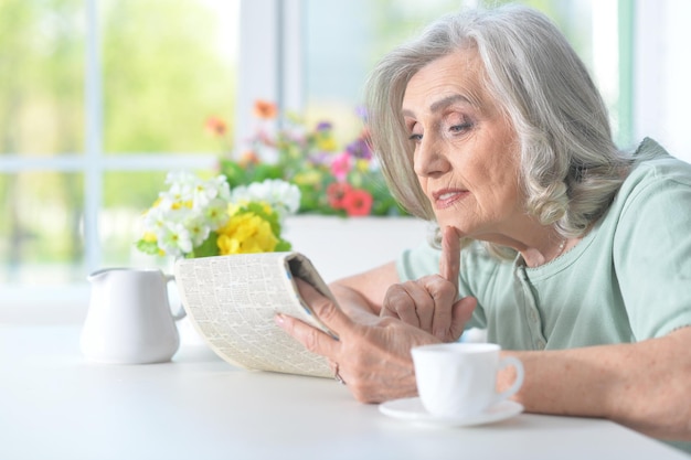 Mooie oude vrouw leest een krant aan een tafel