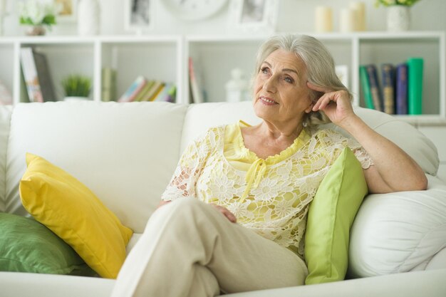 Mooie oudere vrouw die thuis op de bank zit