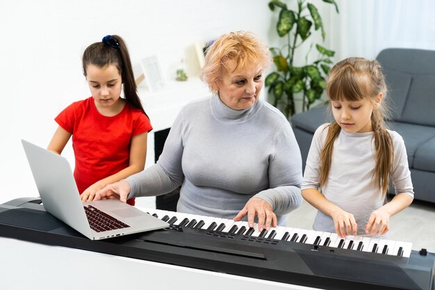 Mooie oudere vrouw leert kleine kleinkinderen synthesizer spelen. Jonge grootmoeder speelt piano voor haar kleinkinderen.