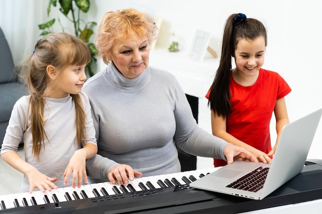 Mooie oudere vrouw leert kleine kleinkinderen synthesizer spelen. Jonge grootmoeder speelt piano voor haar kleinkinderen.