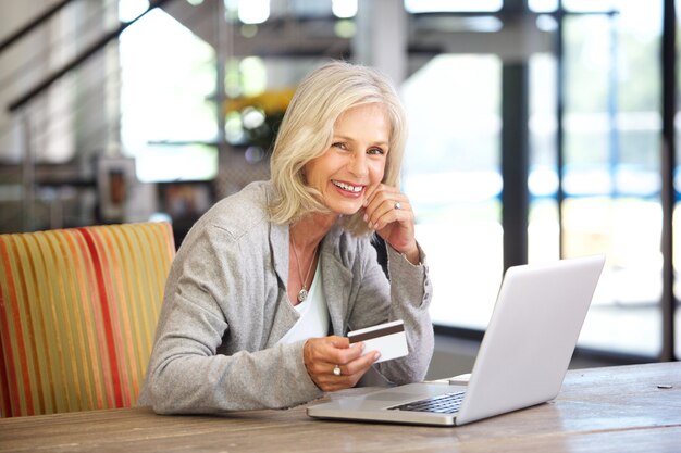 Mooie oudere vrouw met laptopcomputer en creditcard