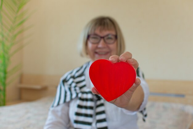 Foto mooie oudere vrouw tegen met een hart in haar handen van haar slaapkamer thuis seniorendag