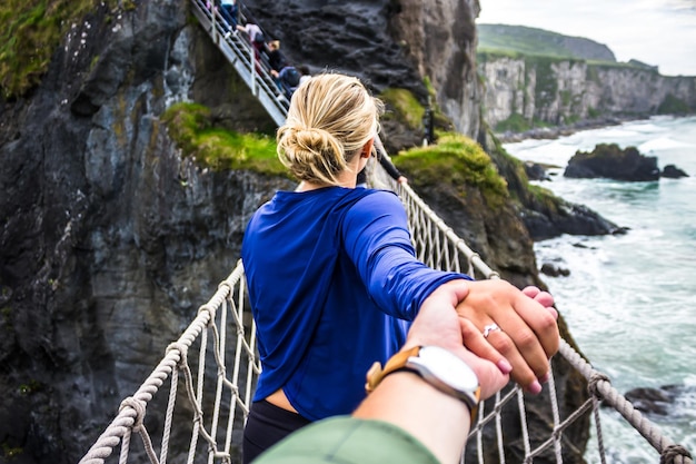 Mooie paar hand in hand en wandelen op de touwbrug van Carrick-a-rede in Noord-Ierland