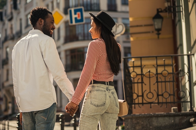 Mooie paar jonge man en vrouw die naar elkaar glimlachen terwijl ze buiten hand in hand gaan tijdens een wandeling