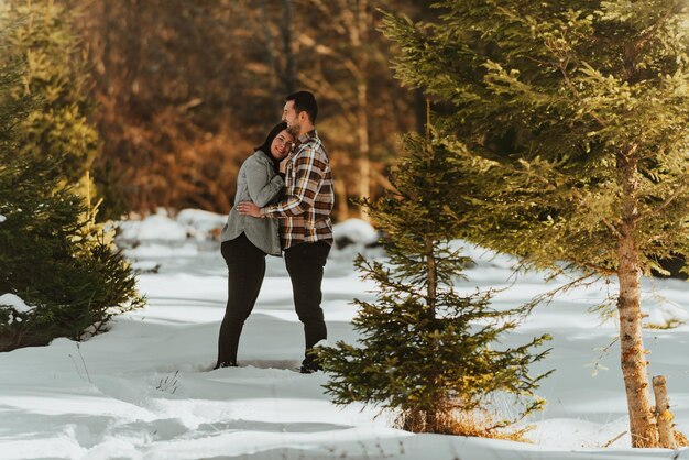 Mooie paar knuffelen tussen besneeuwde dennen vrouw in vrijetijdskleding hand in hand op de borst van de man Selectieve focus