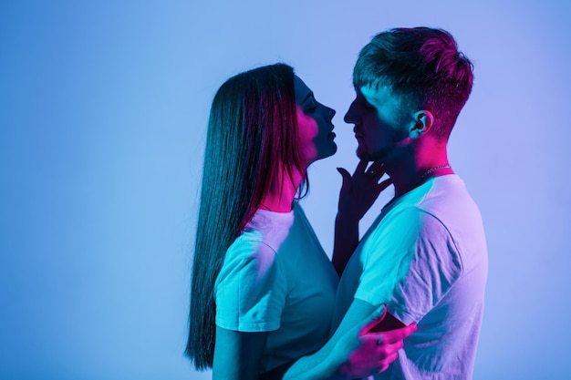 Mooie paar mensen verliefd op creatief kleurrijk blauw en roze licht. Vrij modieuze vrouw met knappe stijlvolle man in witte t-shirts zoenen in studio