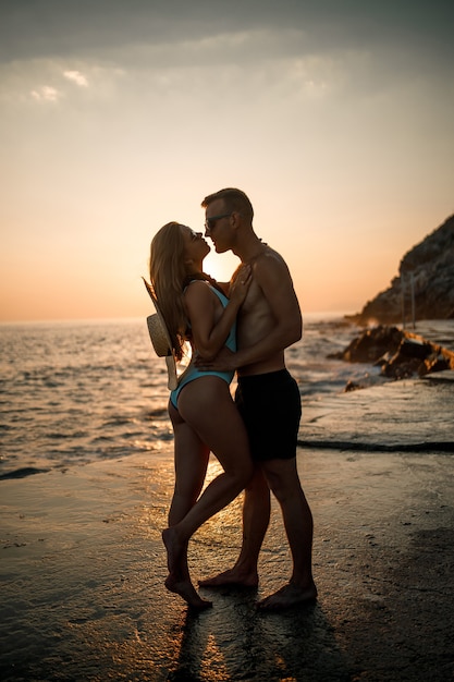 Mooie paar verliefd op de achtergrond van de zonsondergang aan zee. Jonge vrouw en man knuffelen aan zee bij zonsondergang