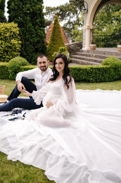 Mooie paar zittend op een plaid op het gras elegante zwangere vrouw met man wachten op