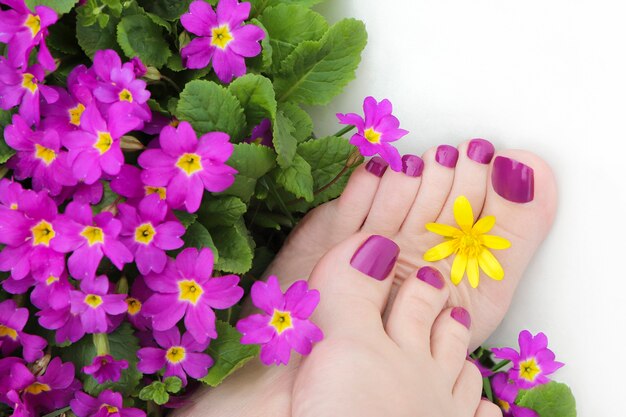 Mooie paarse pedicure op vrouwenvoeten met bloemen op een witte achtergrond.