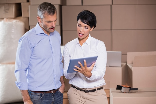 Mooie pakhuismanager die tabletpc met collega met behulp van