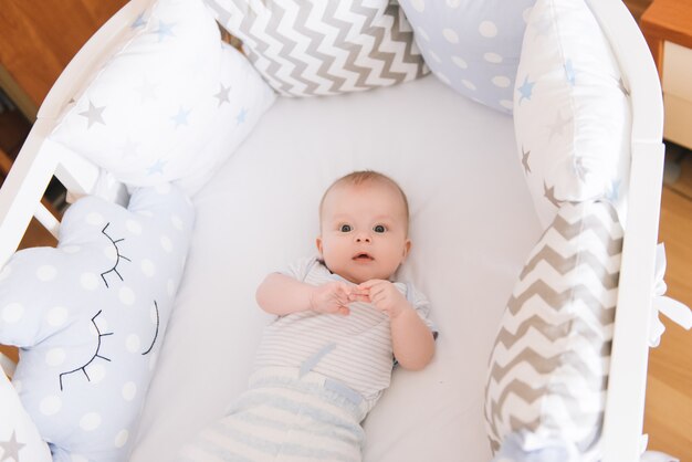 Mooie pasgeboren baby liggend in een ovaal bed met mooie bumpers in delicate grijze, blauwe, witte tinten