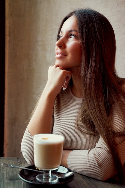 Mooie peinzende gelukkige meisjeszitting in koffie