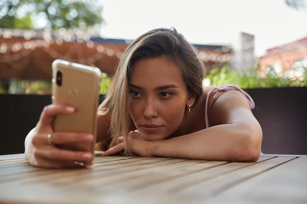 Mooie peinzende melancholische aziatische dame die in café ligt met smartphone