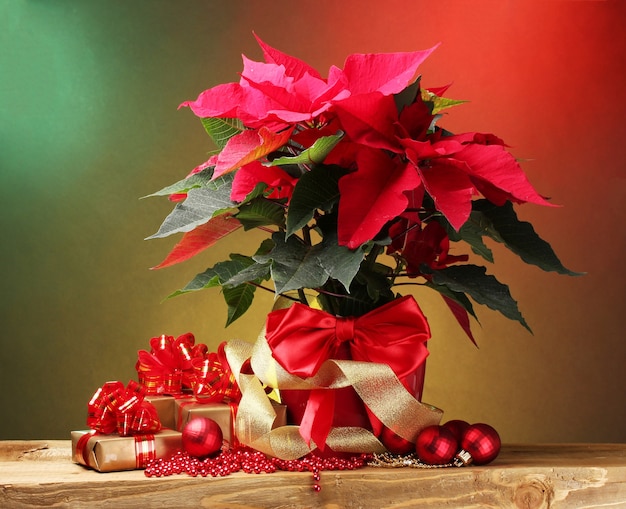 Mooie poinsettia in bloempot, geschenken en kerstballen op houten tafel op lichte achtergrond