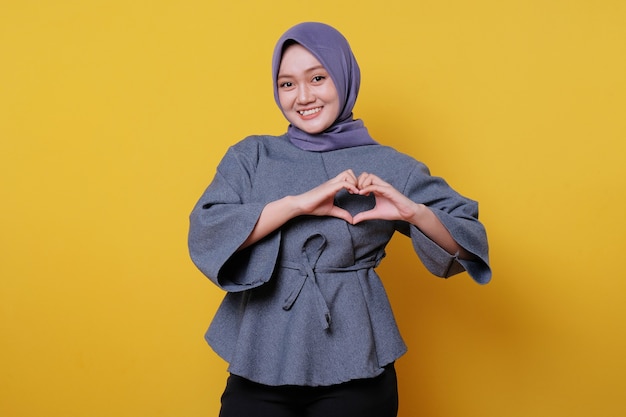Mooie positief vriendelijk ogende jonge vrouw die hijab draagt met een mooie oprechte glimlach die dankbaar en dankbaar voelt, geeft liefdesgebaar