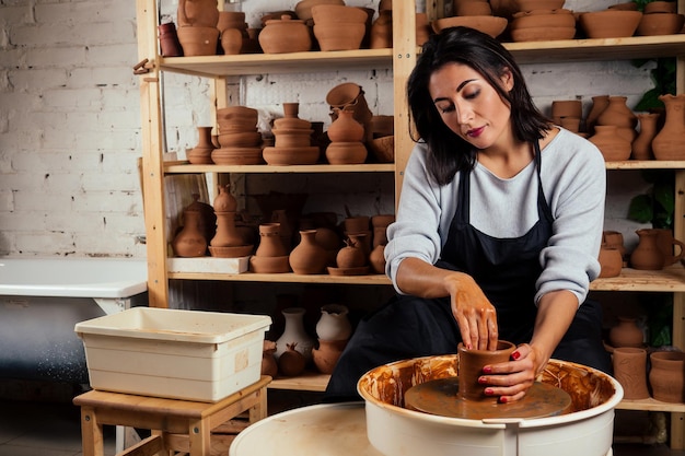 Mooie pottenbakkersmaster vrouw mallen van aarden pot in mastre. vrouwelijke student beeldhouwer werkt met klei op een pottenbakkersschijf en aan de tafel met de tools In werkplaats. inspiratie en creativiteit