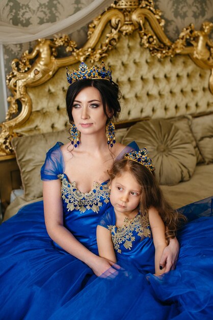 Mooie prinses moeder en dochter in een gouden kroon en luxe blauwe jurken