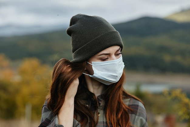 Mooie reiziger met een medisch masker en hoed op de natuur in de bergen