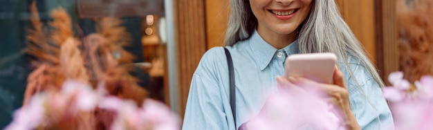 Mooie rijpe Aziatische vrouw in denim overhemd gebruikt mobiele telefoon op terras