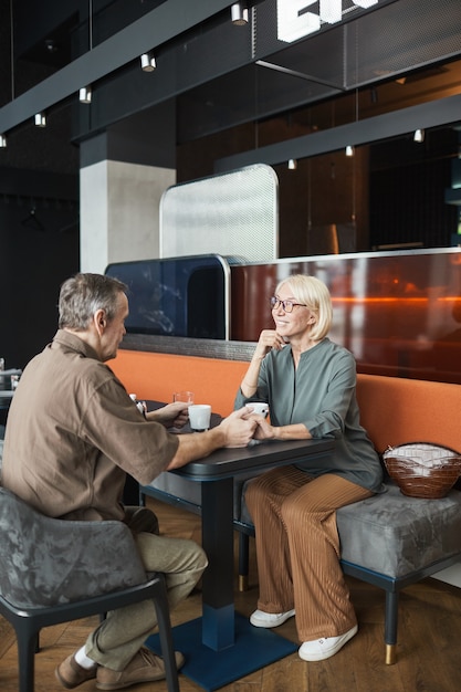 Mooie rijpe vrouw met blond haar aan tafel zitten en luisteren naar vriendje tijdens date in restaurant