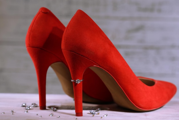 Mooie ring op de hiel van rode vrouwelijke schoen, op houten achtergrond