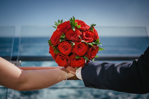 Mooie rode bruiloft boeket van rode rozen, bedrijf met handen op de achtergrond van de zee. Huwelijk