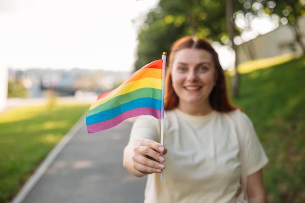 Mooie rode lesbische vrouw met Lgbt-regenboogvlag bij zonsondergang op groene natuur achtergrond Geluk vrijheid en liefde concept voor paren van hetzelfde geslacht