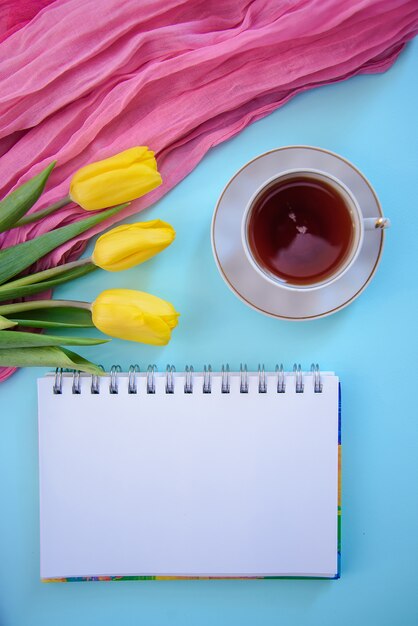 Mooie romantische foto met Kladblok, thee en tulpen op blauwe achtergrond