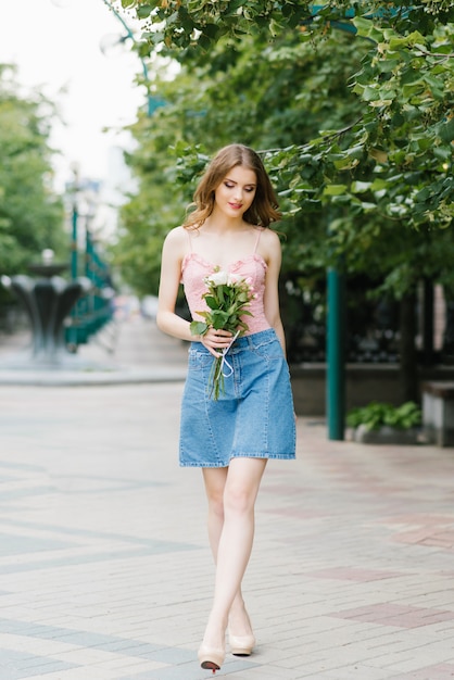 mooie romantische jonge vrouw in een korte denim rok houdt een boeket rozen in haar handen