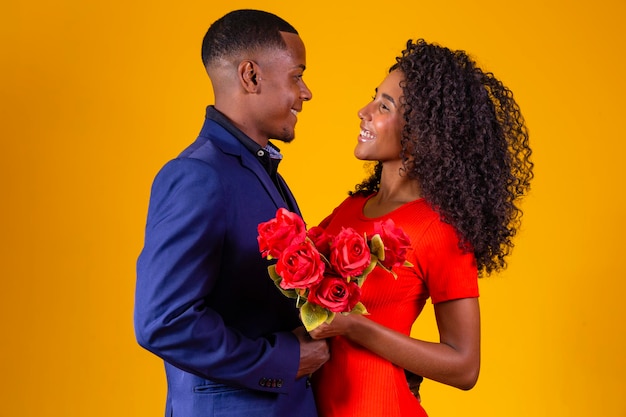 Mooie romantische paar geïsoleerd op gele achtergrond Aantrekkelijke jonge vrouw in rode jurk met rode rozen en knappe man in een pak zijn verliefd Happy Valentine's Day