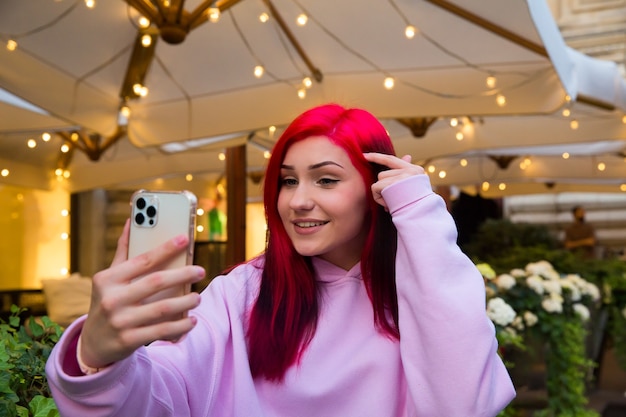 Mooie roodharige influencer blogger meisje in café praten video-oproep met behulp van smartphone met haar abonnees in sociale netwerken.