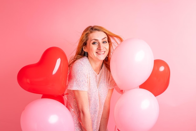 Mooie roodharige meisje met rood hart ballon poseren Happy Valentines Day concept Studio foto van mooie gember meisje dansen op roze achtergrond