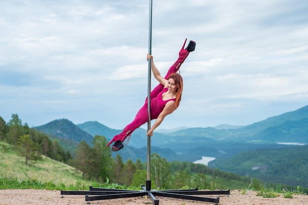 Mooie roodharige vrouw dansen op een draagbaar platform op een achtergrond van bergen Het meisje beweegt seksueel naast de paal Jumpsuit voor lessen hoge hakken Altai Geweldige flexibiliteit