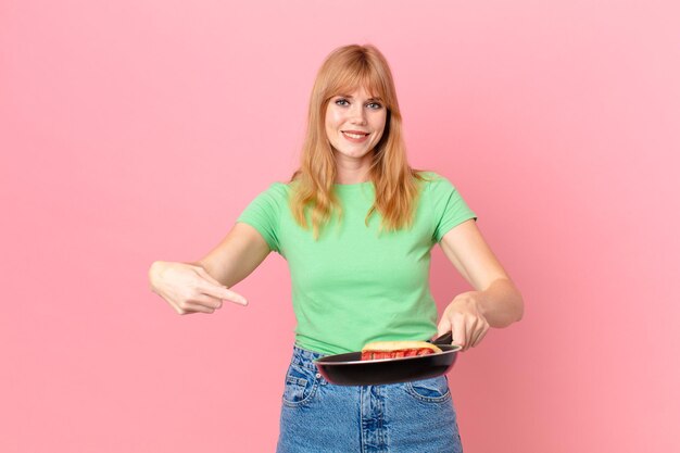 Mooie roodharige vrouw die een hotdog kookt met een pan