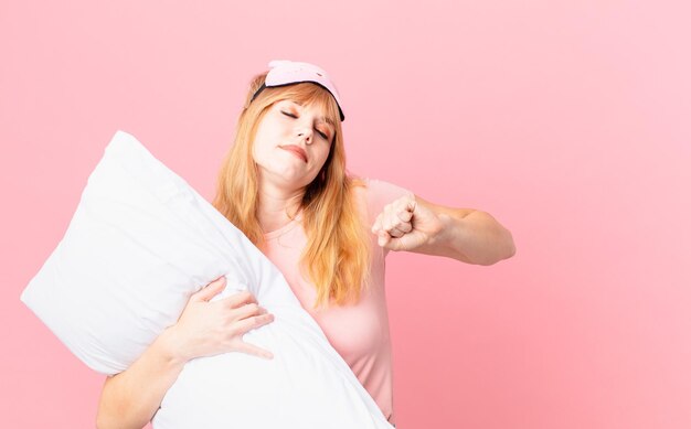 Mooie roodharige vrouw die een pyjama draagt en een kussen vasthoudt