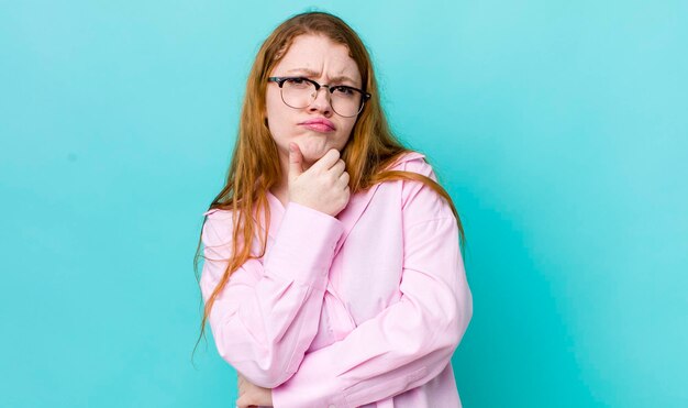 Mooie roodharige vrouw die er ernstig verward uitziet, onzeker en bedachtzaam twijfelt tussen opties of keuzes