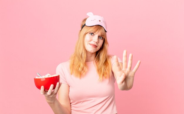 Mooie roodharige vrouw die lacht en er vriendelijk uitziet, met nummer vier in een pyjama en met een vlokkenkom