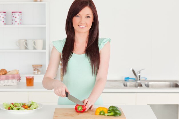 Mooie roodharige vrouw die sommige groenten in de keuken snijdt