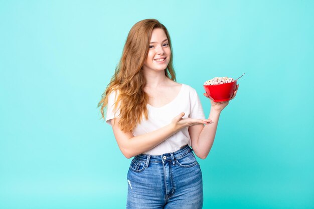 mooie roodharige vrouw die vrolijk lacht, zich gelukkig voelt en een concept toont en een ontbijtkom vasthoudt