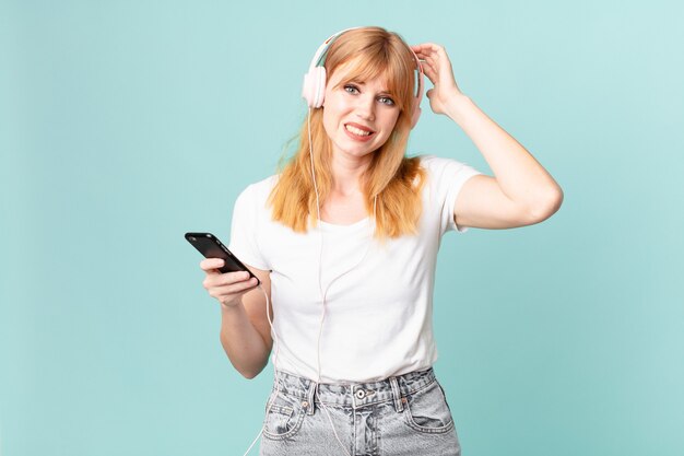 Mooie roodharige vrouw die zich gestrest, angstig of bang voelt, met de handen op het hoofd en naar muziek luistert met een koptelefoon