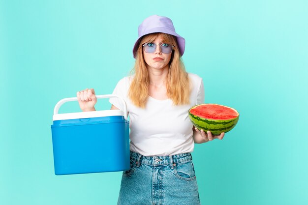 Mooie roodharige vrouw met een draagbare koelkast en een watermeloen