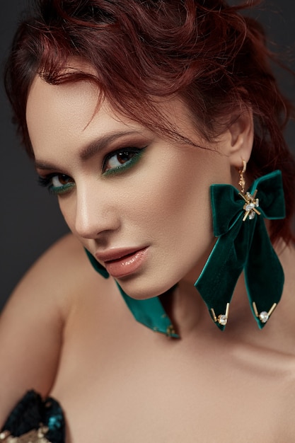 Mooie roodharige vrouw met make-up en groene oorbellen
