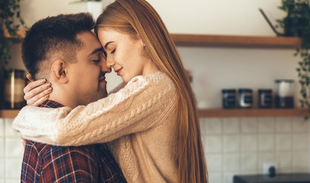 Mooie roodharige vrouw met sproeten omarmd door haar minnaar heeft een intiem moment in de keuken