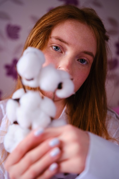 Mooie rooiharen vrouw in de twintig met naakt make-up witte katoenbloemen op paarse bloemen achtergrond huidverzorging gezondheidszorg cosmetische procedures concept